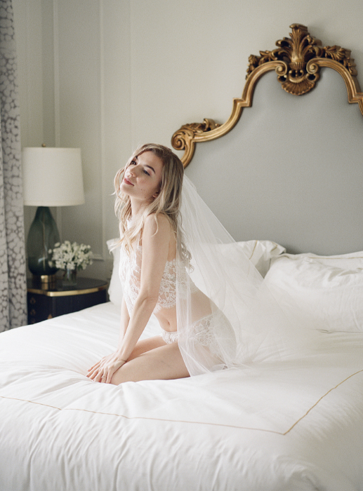 Bride in lace and veil on white bed with gilded headboard